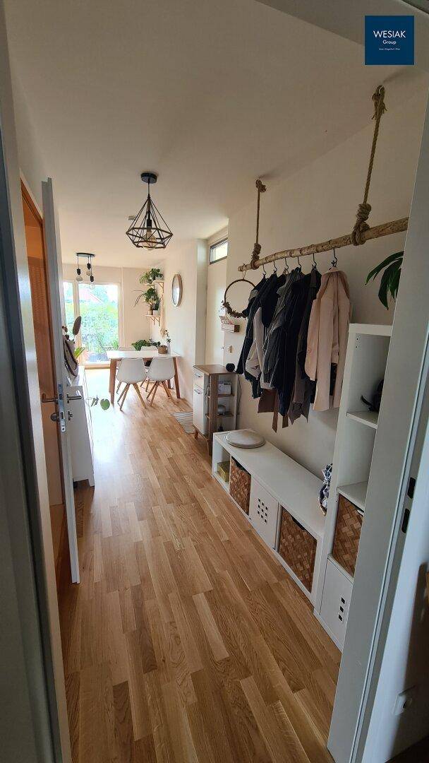 Heller Flur mit Holzboden und Garderobe, der in einen offenen Essbereich führt.