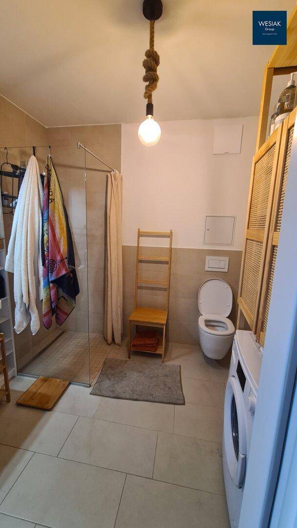 Modernes Badezimmer mit Dusche, WC und Waschmaschine, hell gefliest.