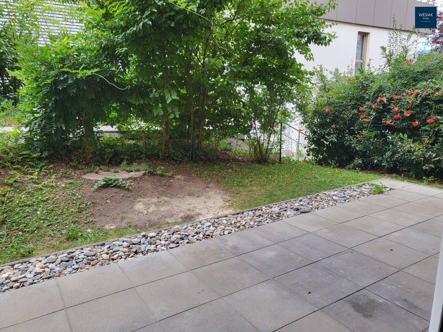 Geräumige Terrasse mit Steinplatten und angrenzendem Gartenbereich mit üppiger Vegetation.
