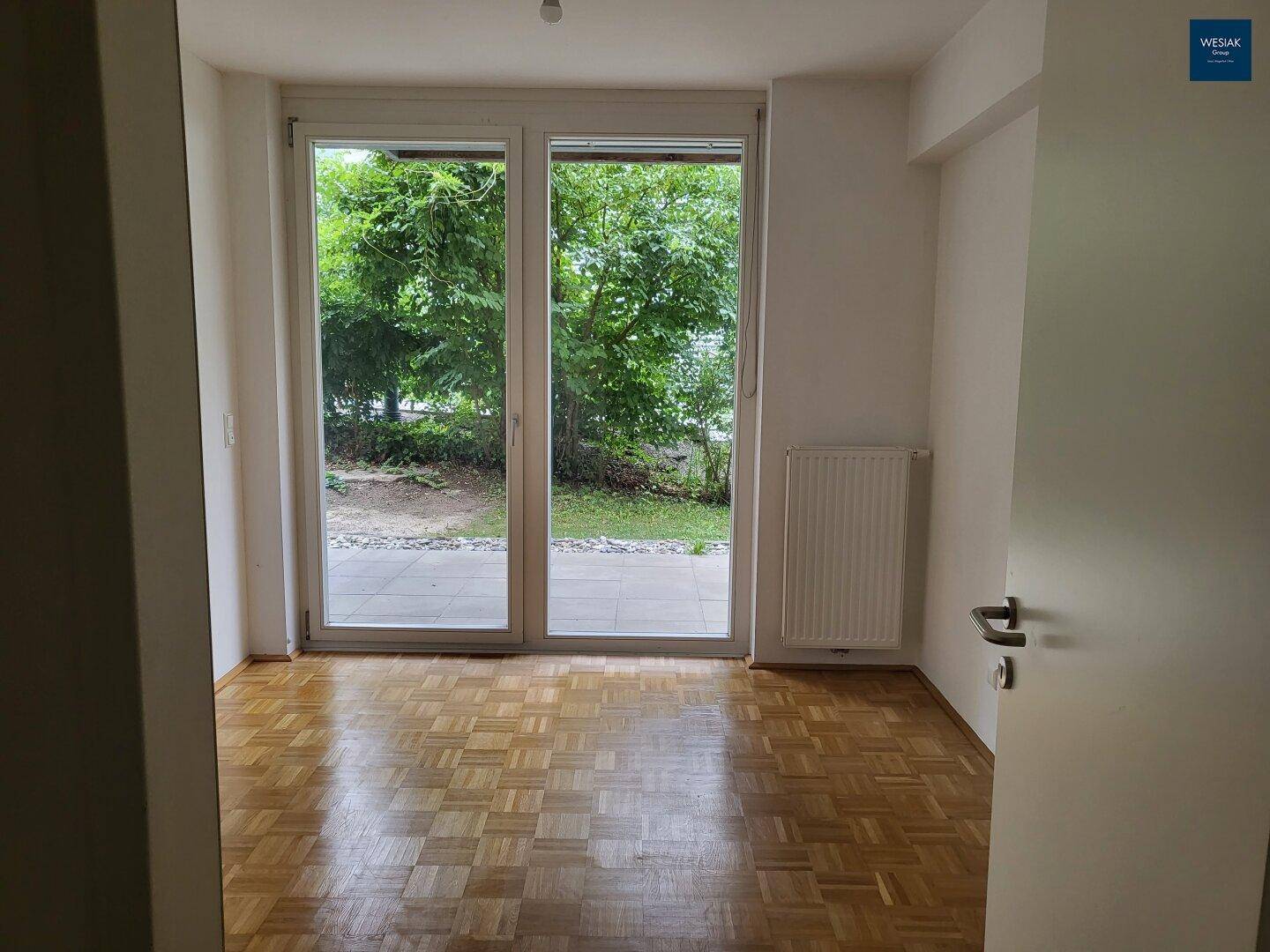 Geräumiges Wohnzimmer mit Parkettboden und großen Glastüren zum Gartenbereich.