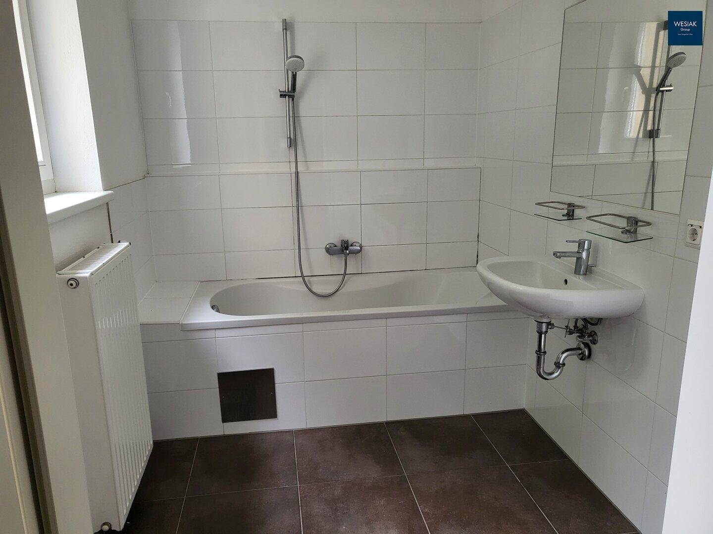 Funktionales Badezimmer mit Badewanne, Waschbecken, weißen Fliesen und Fenster.