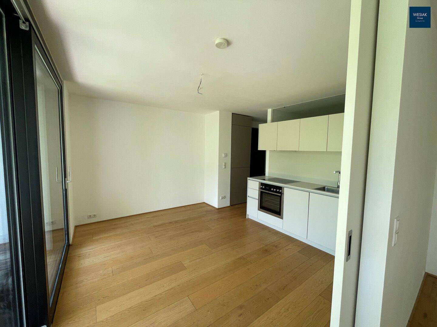 Heller Wohnbereich mit Holzboden und integrierter Küchenzeile, ideal für offenes Wohnen.