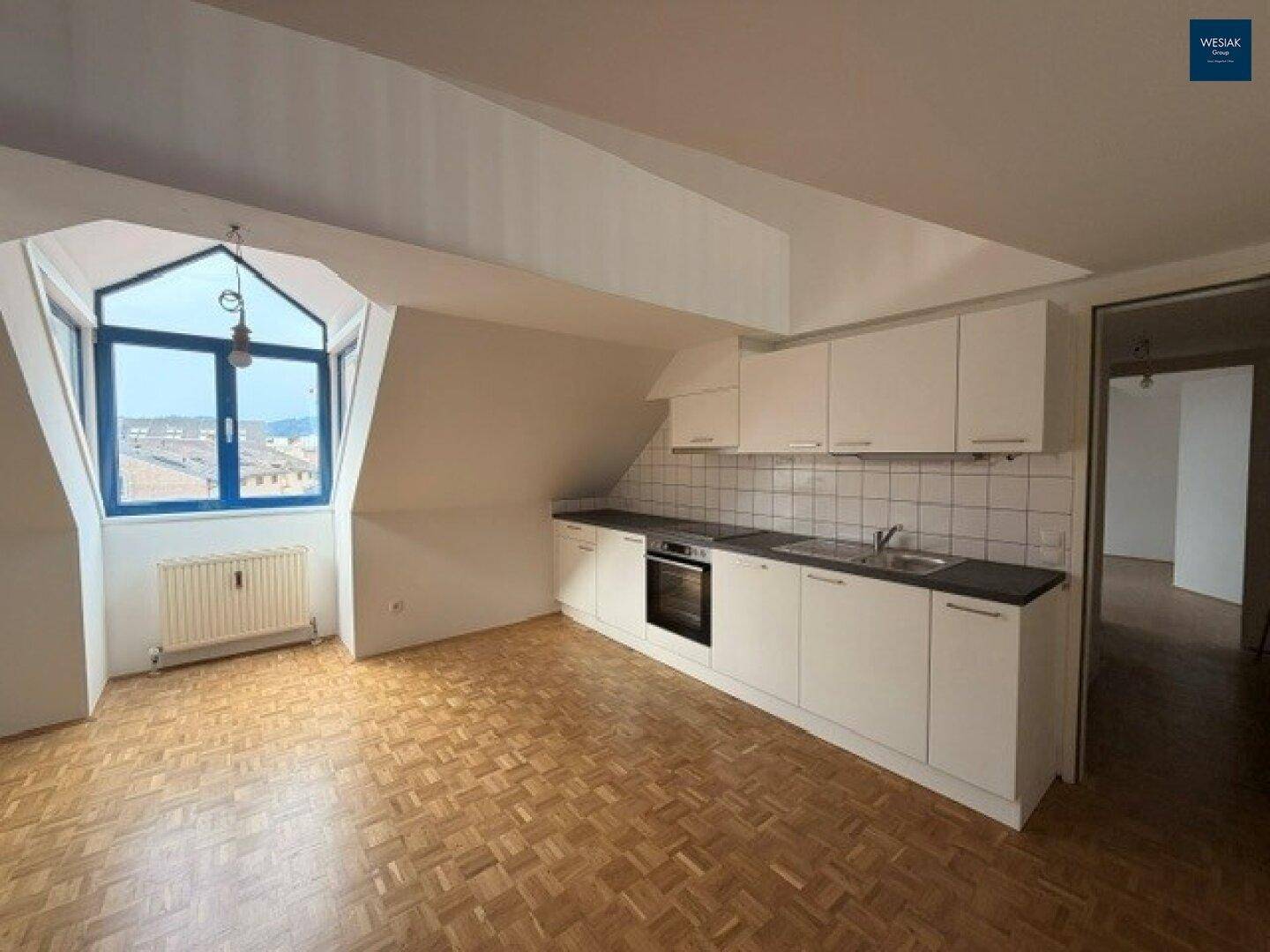 Dachgeschosswohnung mit kleiner Küchenzeile, Parkettboden und charakteristischem Fenster mit Ausblick.