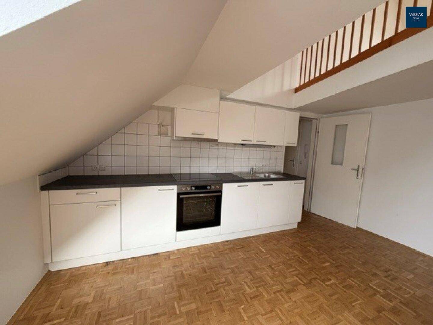 Funktionale Küchenzeile in einem Dachgeschossraum mit Holztreppe und Parkettboden, ideal für Singles.