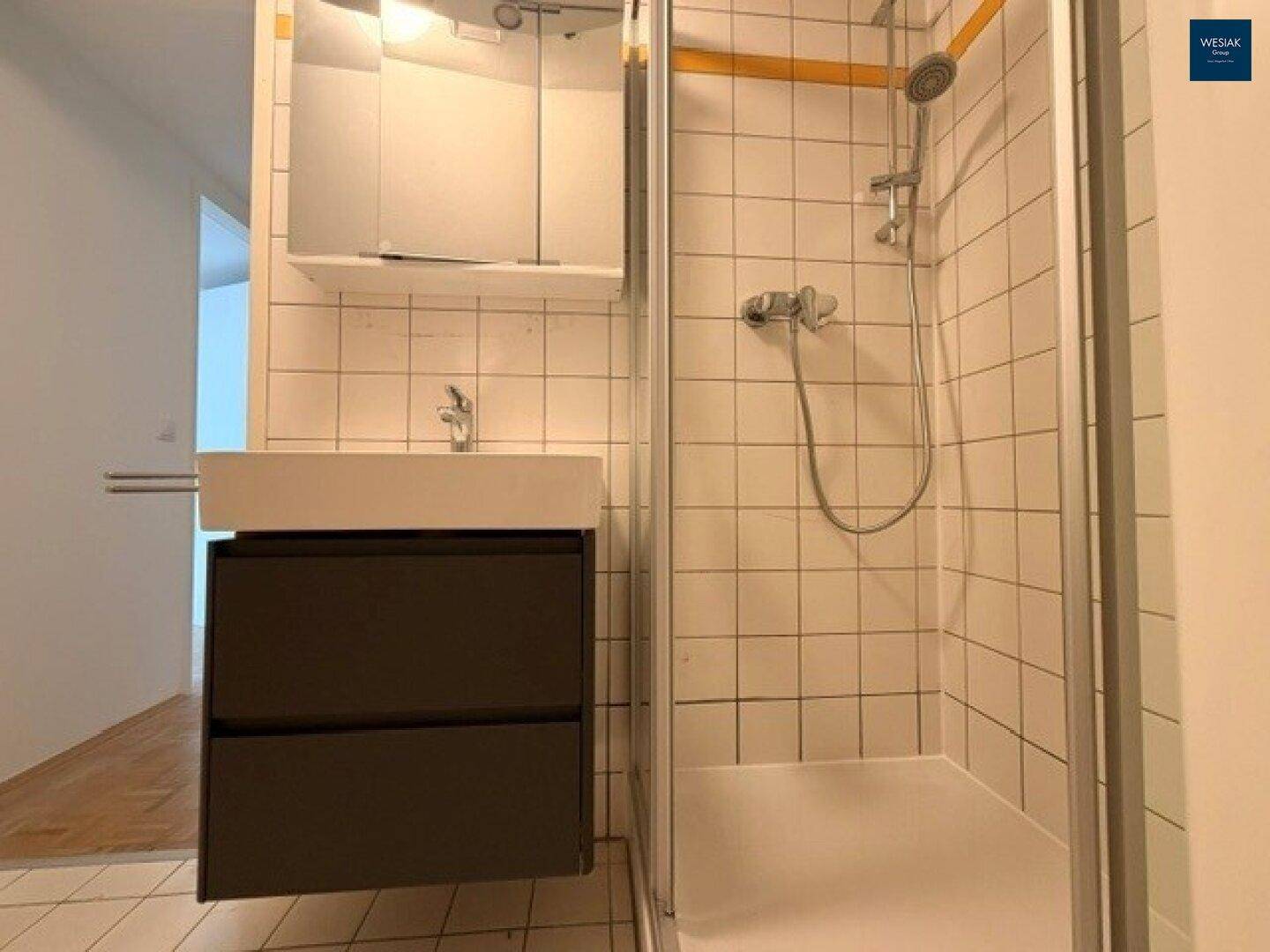 Detaillierte Ansicht des Badezimmers mit Waschbecken, Spiegel und Duschkabine, funktional und hell.