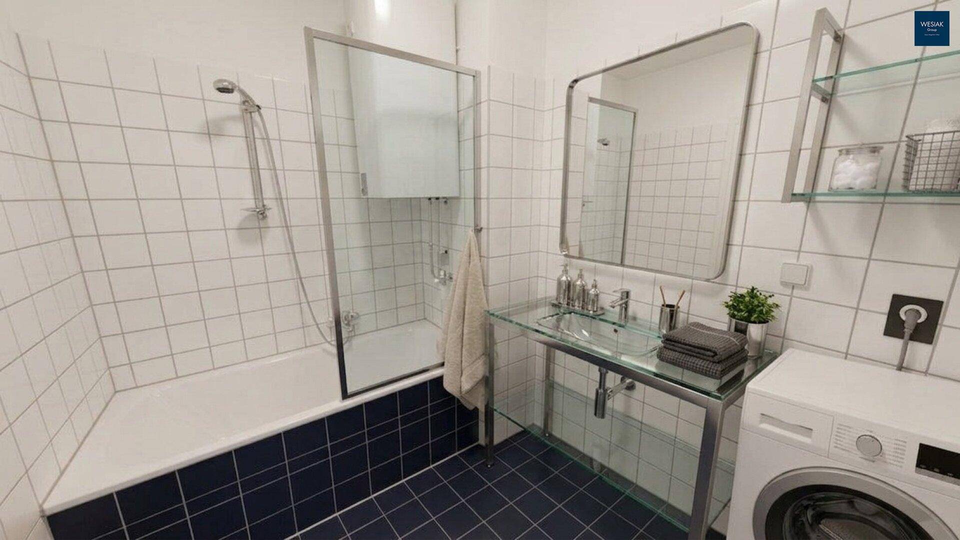 Helles Badezimmer mit Badewanne, Dusche und Waschmaschine in weiß-blauer Fliesenoptik.
