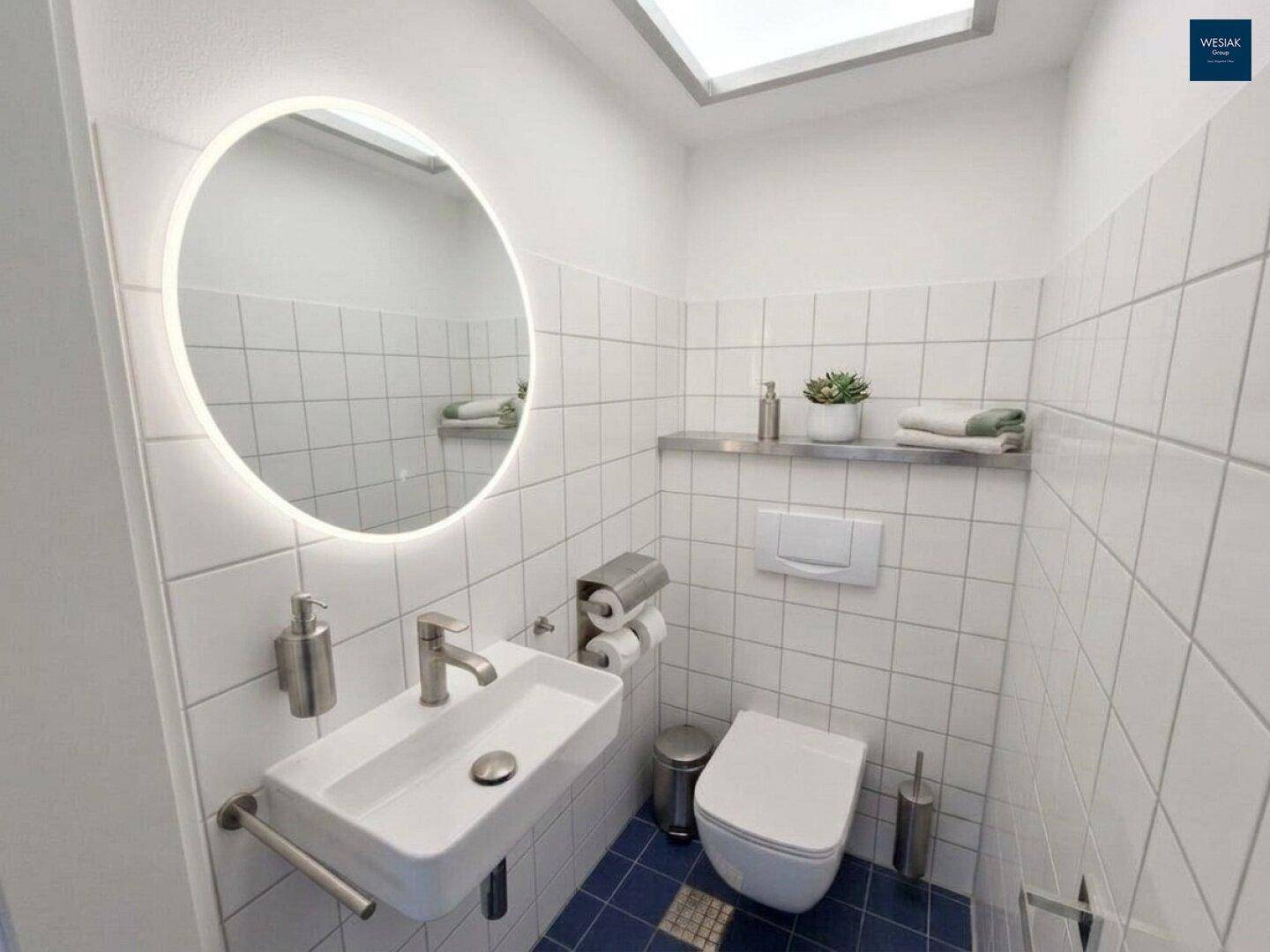 Kompaktes Gäste-WC mit modernem Waschbecken, beleuchtetem Spiegel und blauen Bodenfliesen.
