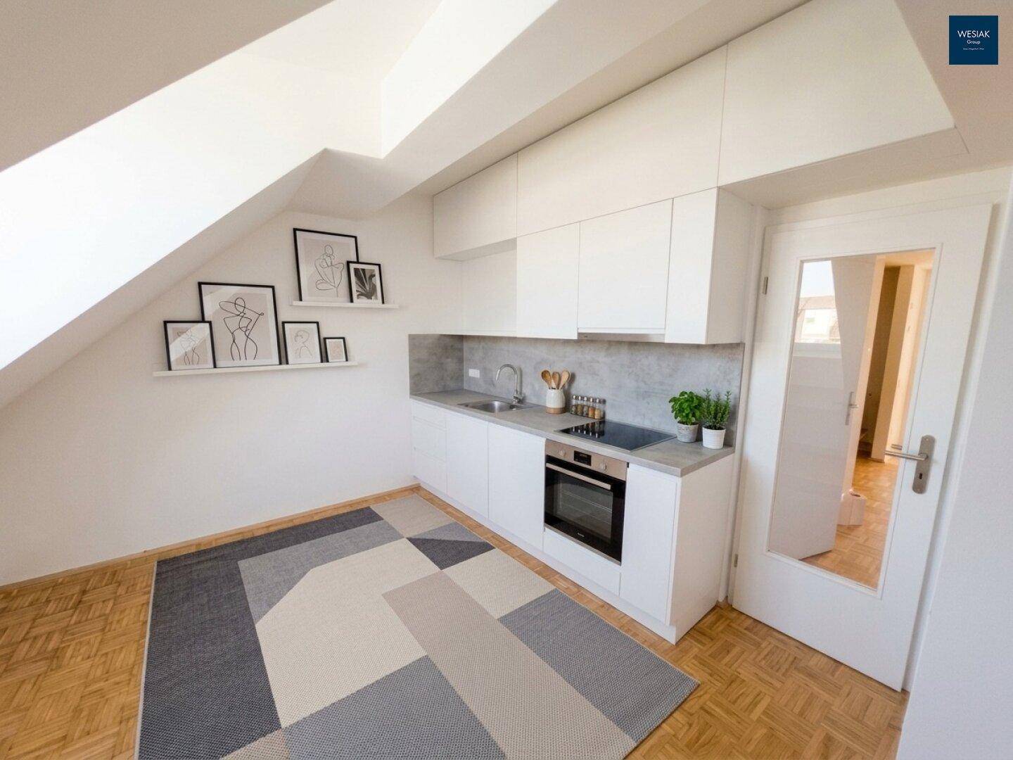Moderne Küchenzeile in Dachgeschosswohnung mit weißen Schränken und schrägen Wänden.