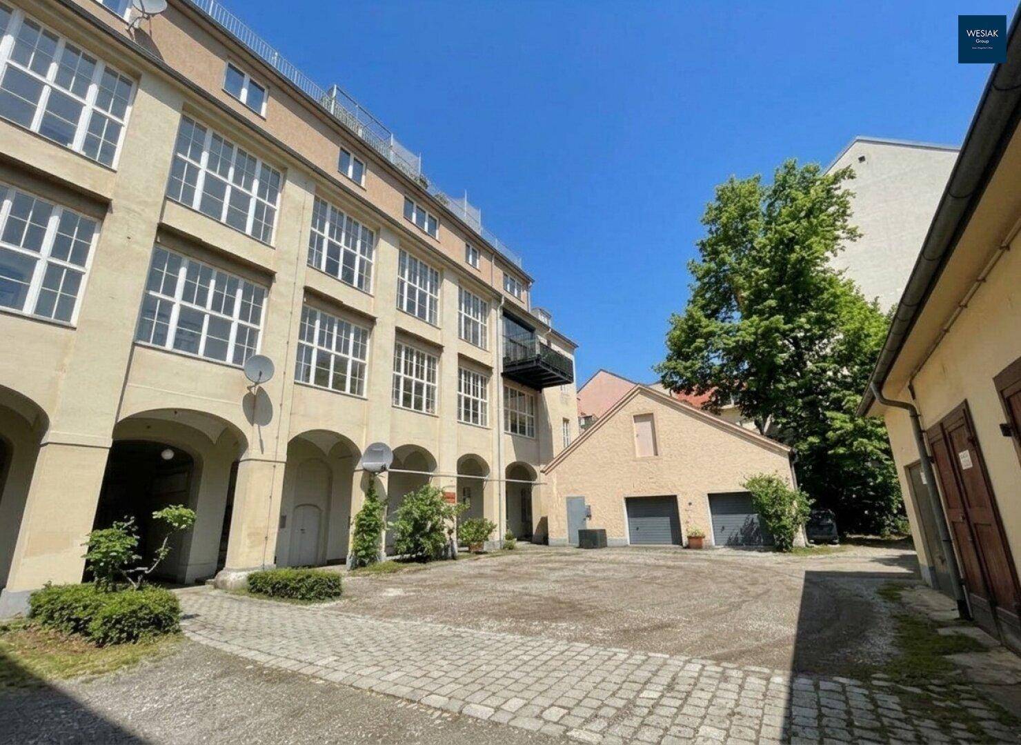Innenhof mit Kopfsteinpflaster, alten Gebäuden und viel Grün unter blauem Himmel.