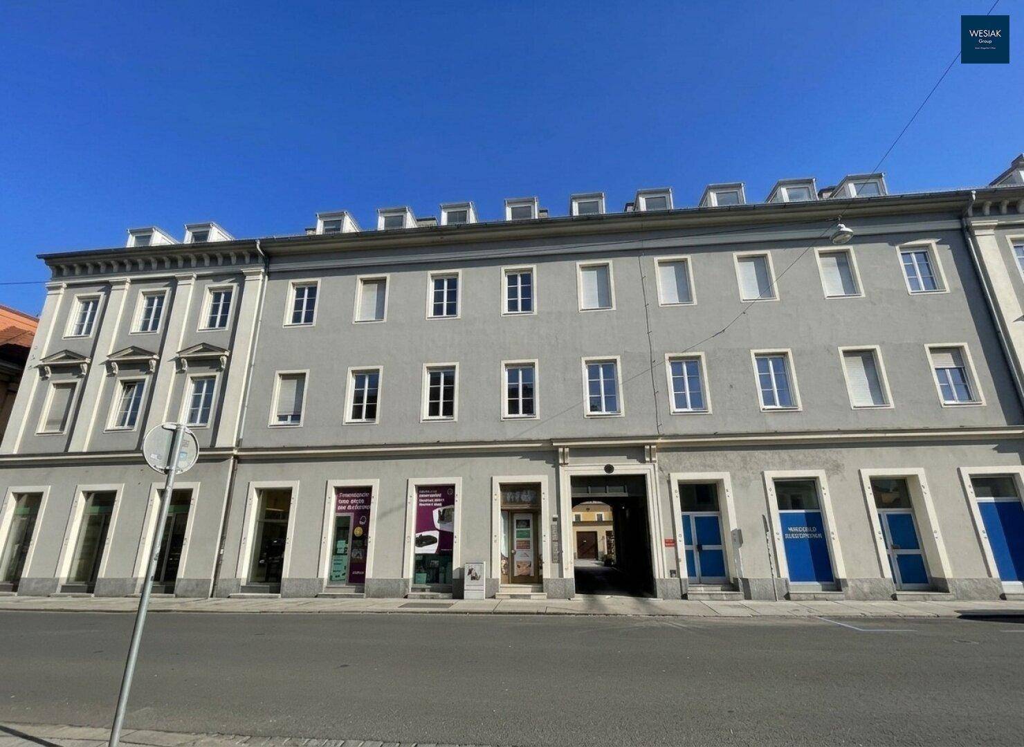 Historisches Gebäude mit grauer Fassade und vielen Fenstern an einer Stadtstraße.