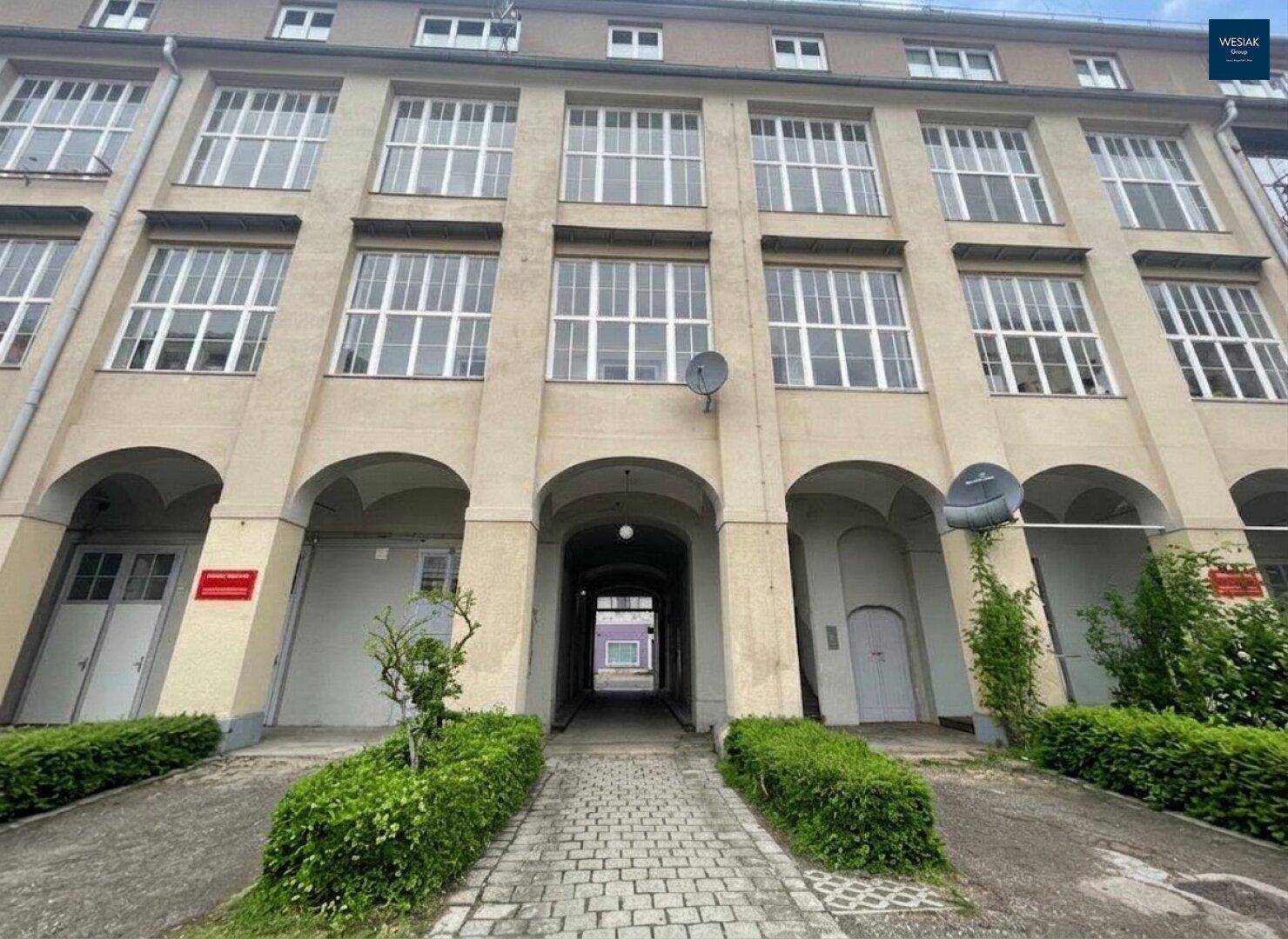 Eingangsbereich eines historischen Gebäudes mit großen Fenstern und Arkaden.