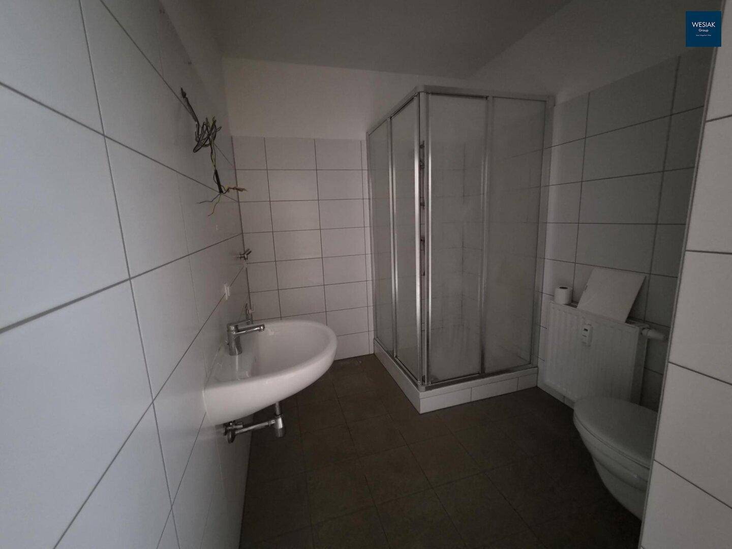 Modernes Badezimmer mit Duschkabine, Waschbecken und WC, komplett gefliest in Weiß.