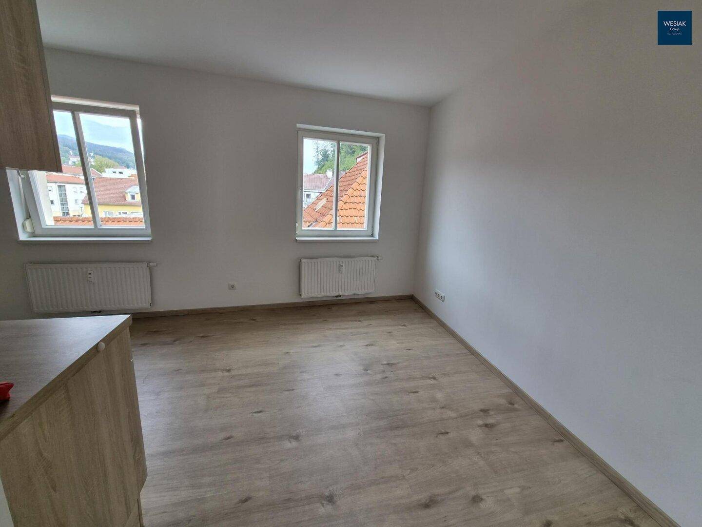 Heller Wohnraum mit Laminatboden und zwei Fenstern, die einen Blick auf die Umgebung bieten.