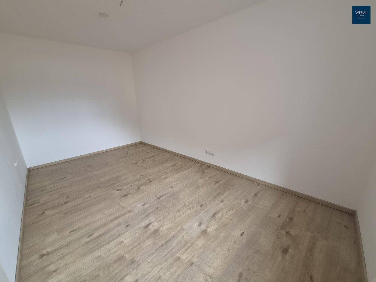 Leeres Zimmer mit hellem Laminatboden und weißen Wänden, bereit zur individuellen Gestaltung.