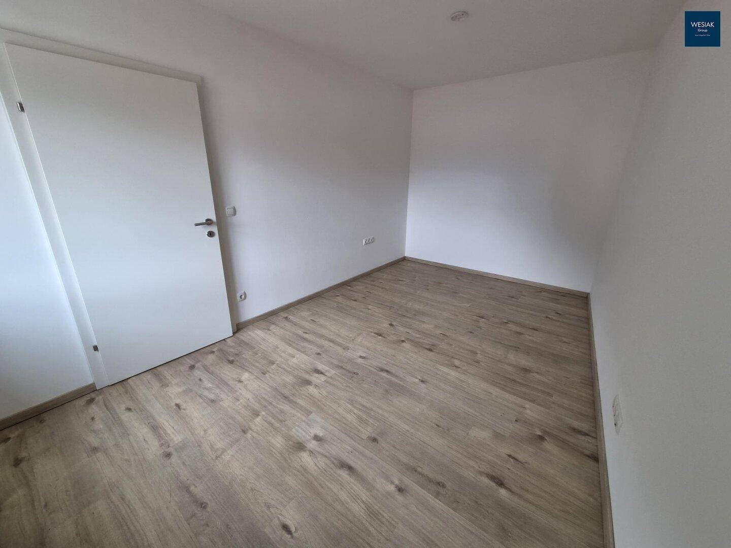 Unmöbliertes Zimmer mit Laminatboden und weißer Tür, ideal als Schlaf- oder Arbeitszimmer.