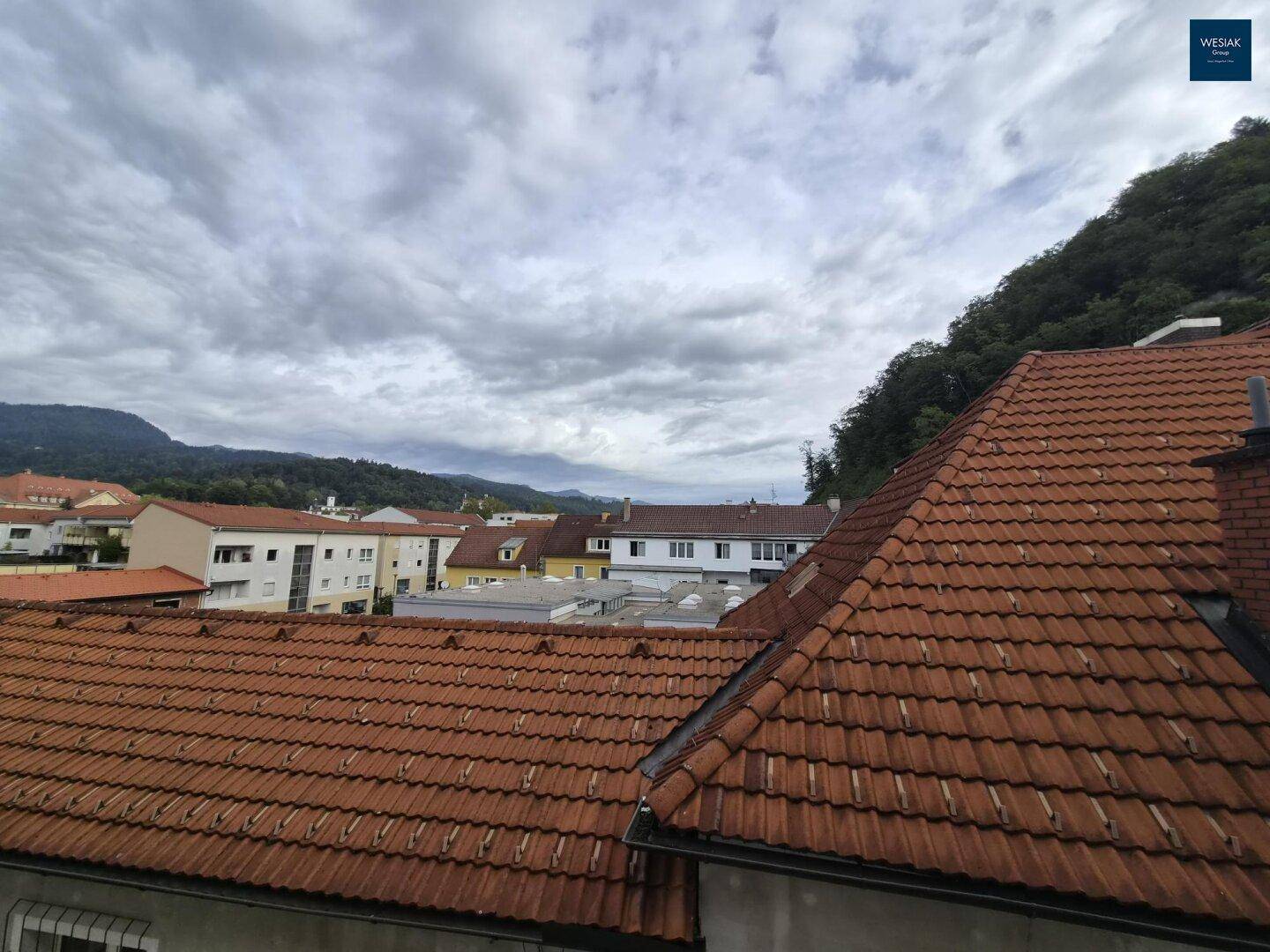 Weitläufiger Blick über die Dächer der Stadt und die umliegende grüne Hügellandschaft.