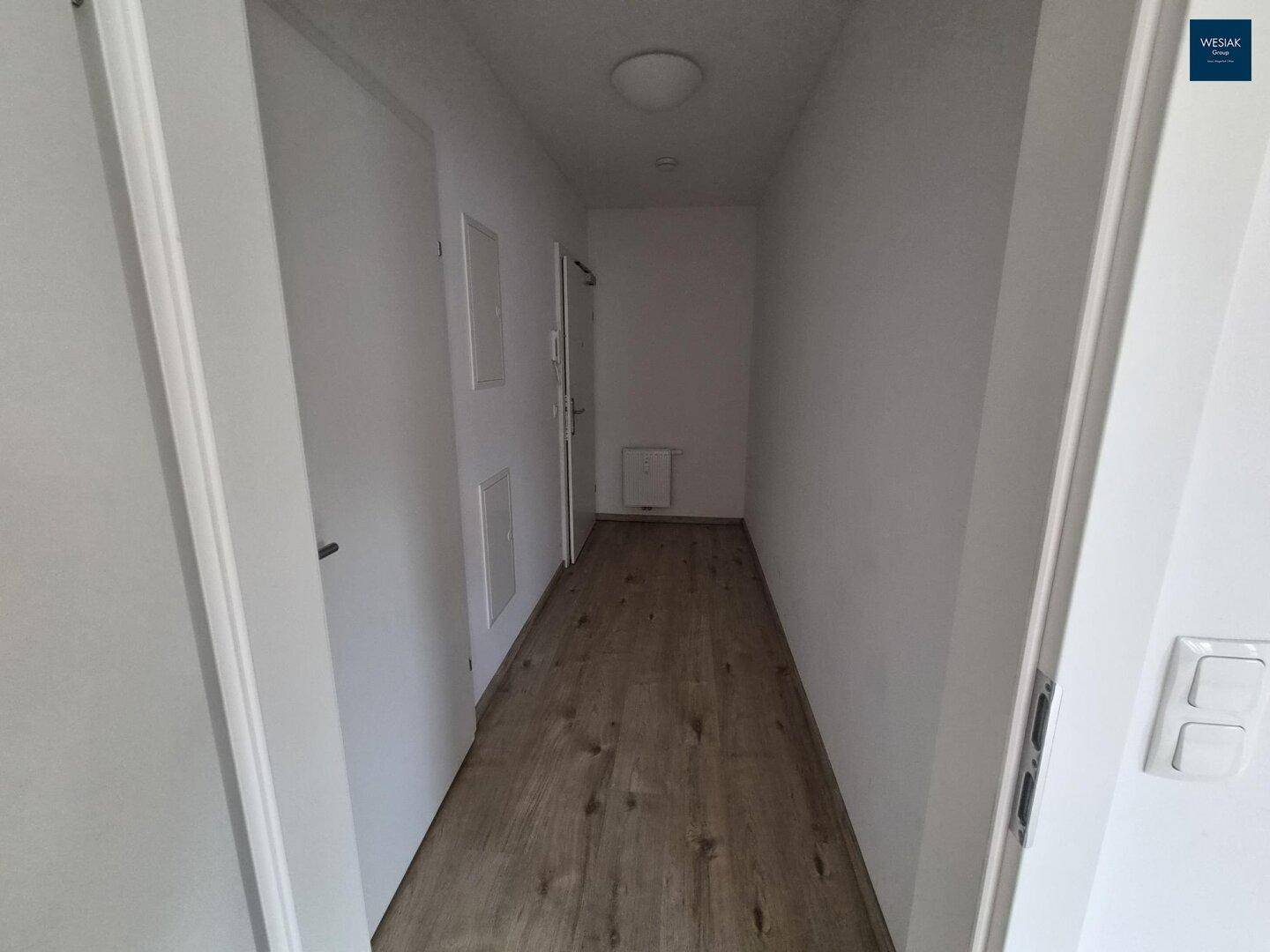 Schmaler, gut beleuchteter Flur mit hellem Laminatboden und weißen Wänden.