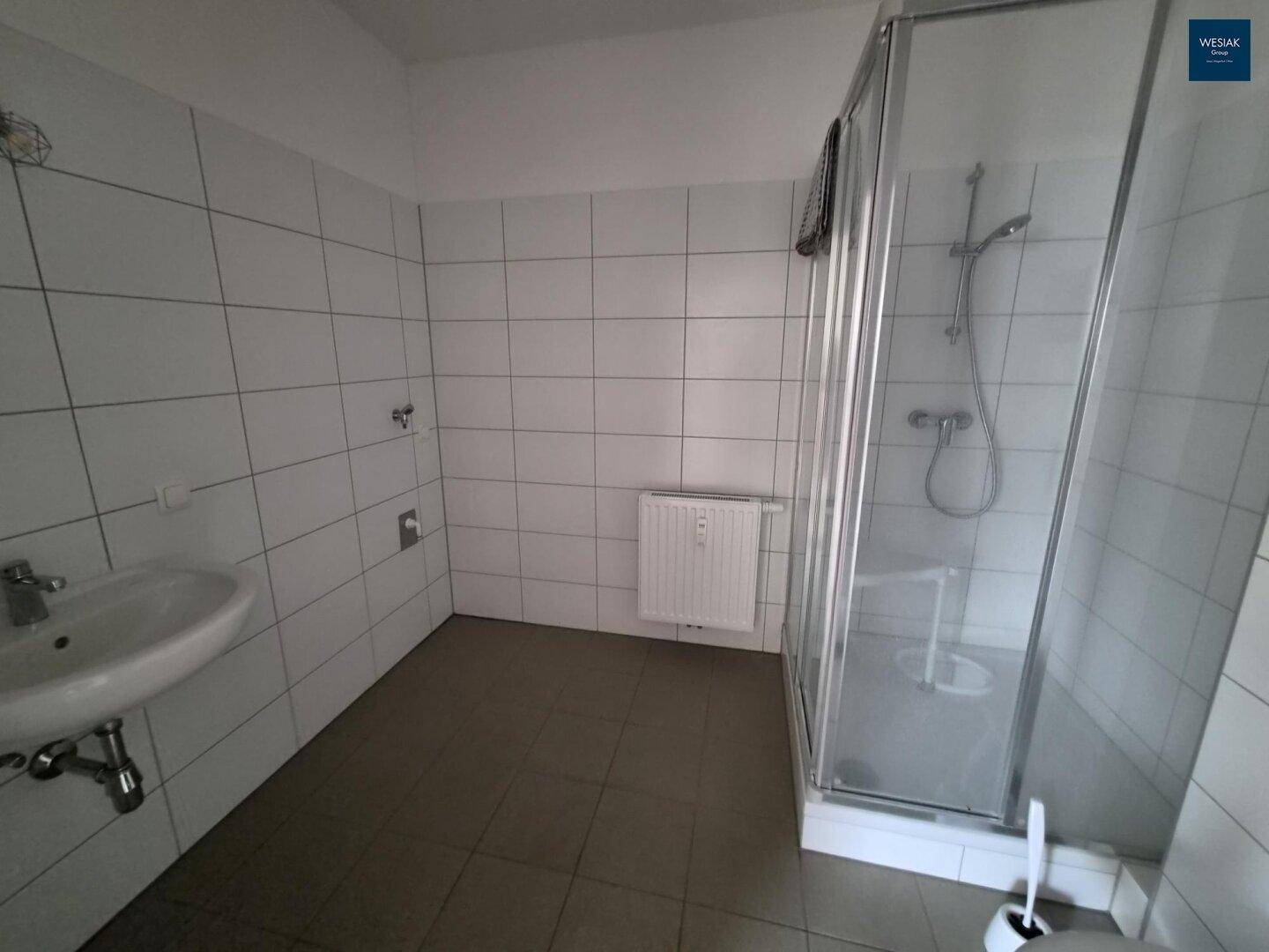 Einfaches Badezimmer mit Duschkabine, Waschbecken und weißen Fliesen.