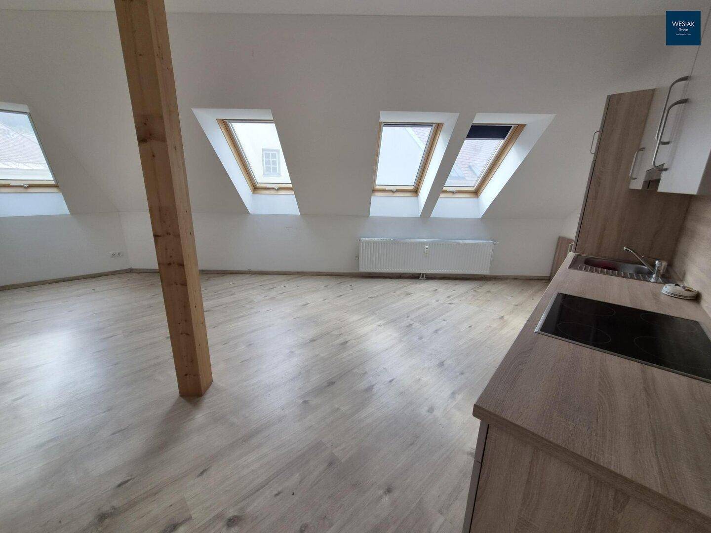 Heller Wohnbereich im Dachgeschoss mit Dachfenstern, Holzbalken und integrierter Küchenzeile.