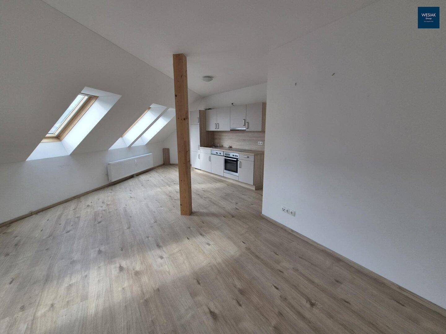Offener Wohnbereich mit integrierter Küchenzeile, Laminatboden und viel Tageslicht durch Dachfenster.