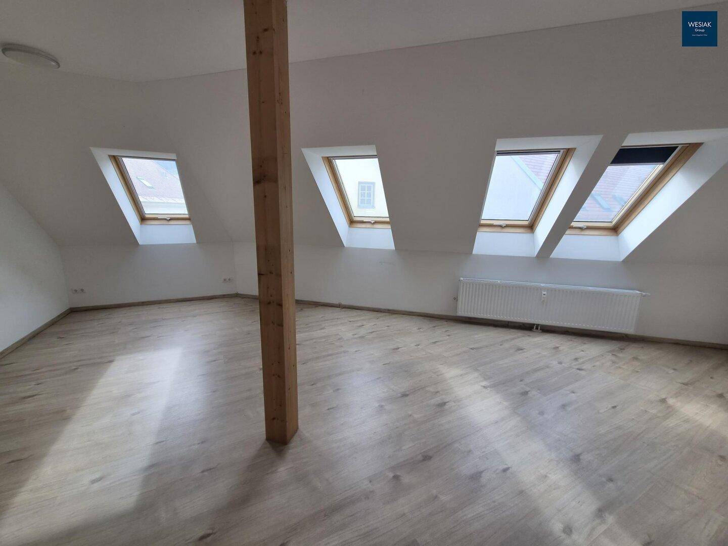 Heller Wohnbereich mit Holzbalken, Laminatboden und mehreren Dachfenstern für viel Licht.
