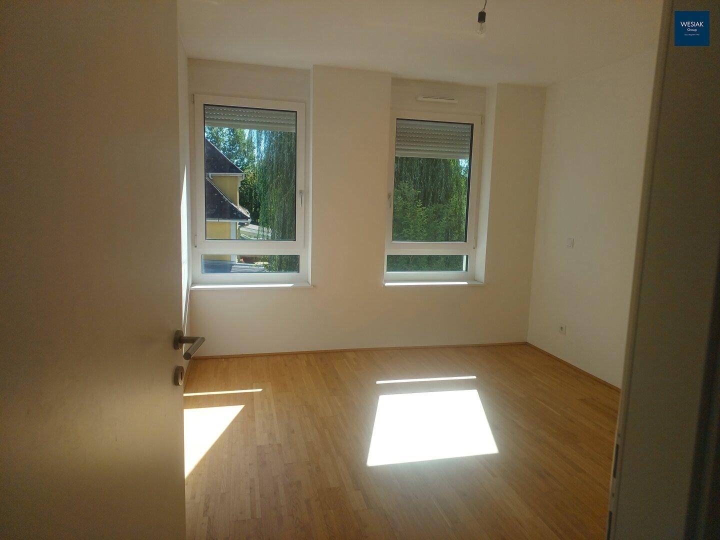 Helles Zimmer mit Holzboden, großen Fenstern und Rollläden, ideal als Schlaf- oder Arbeitszimmer.