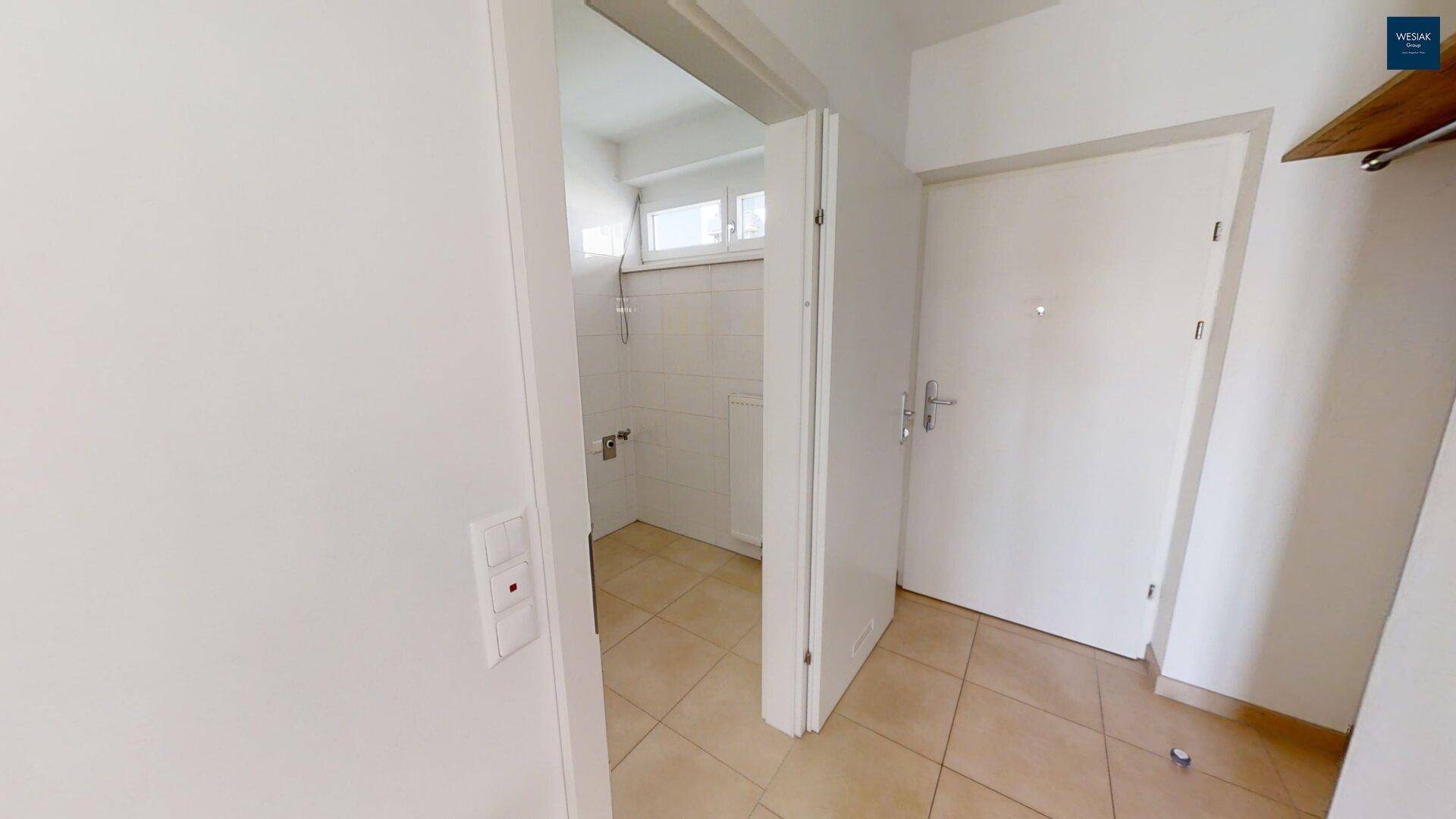 Flur mit Fliesenboden und Zugang zu einem Badezimmer mit Duschbereich.