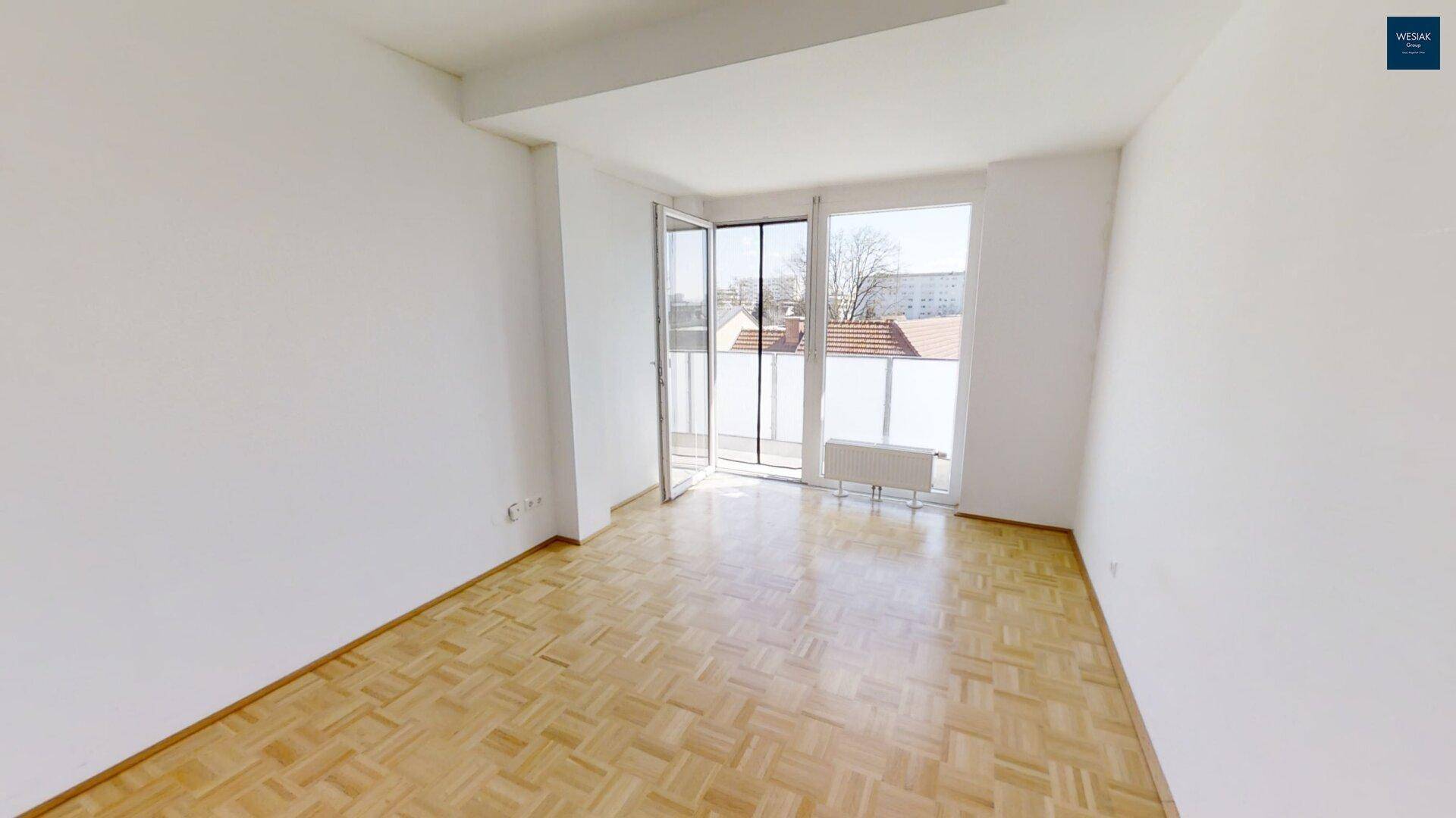 Helles Wohnzimmer mit Parkettboden und Zugang zu einem sonnigen Balkon.
