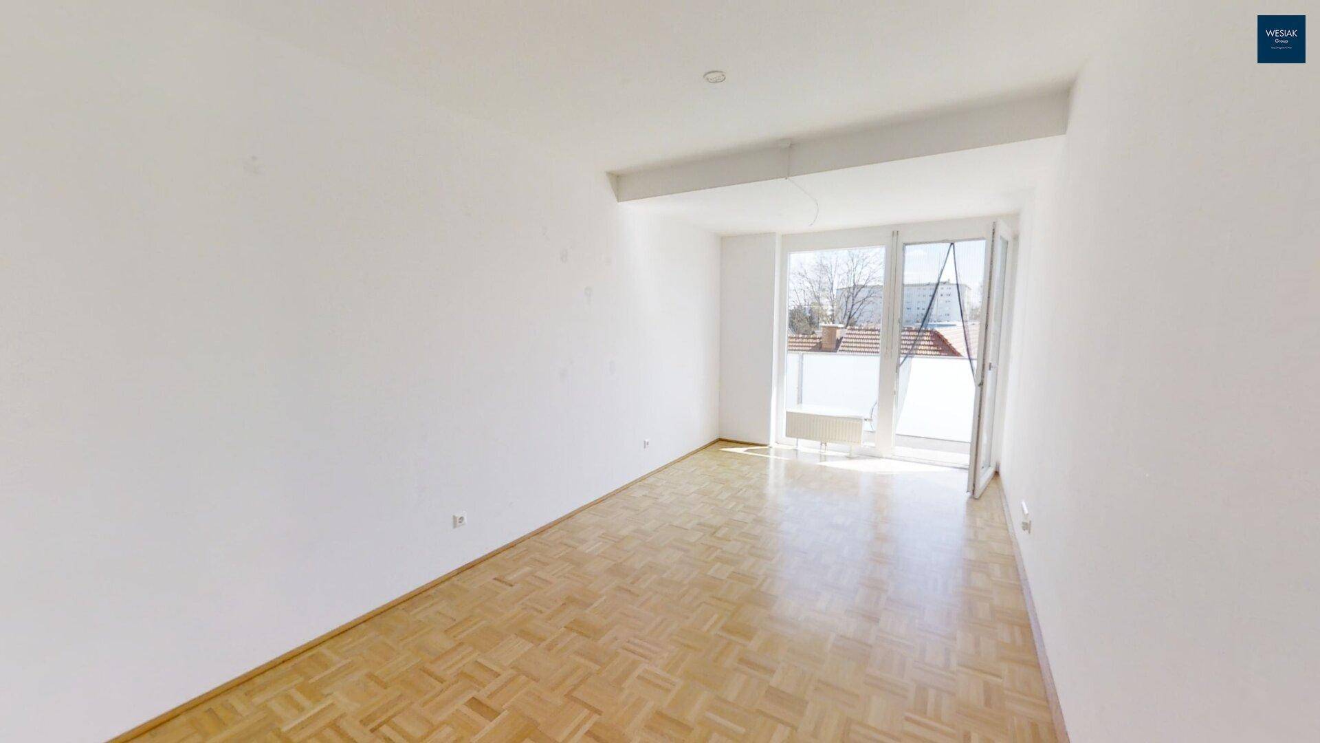 Geräumiges Wohnzimmer mit Parkettboden und großen Fenstern zum Balkon.