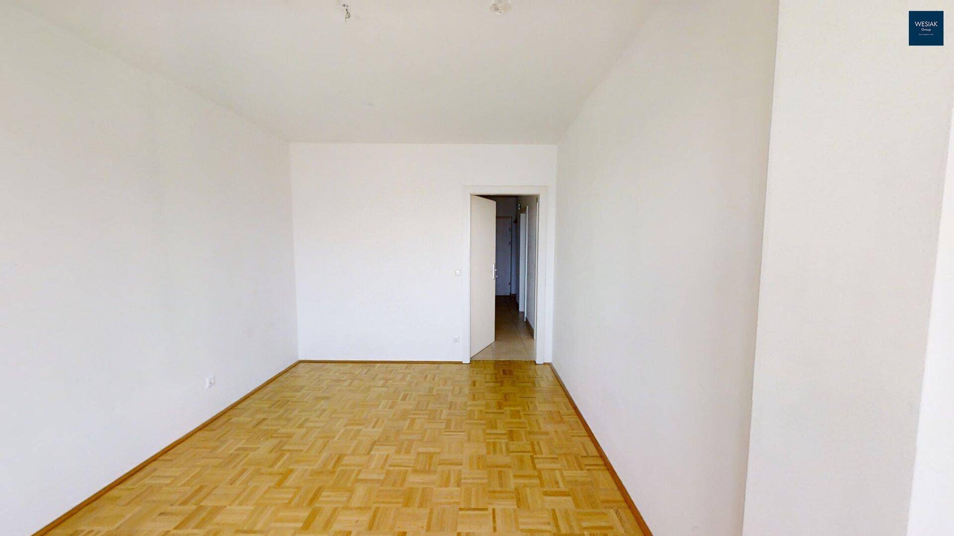 Leeres Wohnzimmer mit Parkettboden und einem Durchgang zu weiteren Räumen.