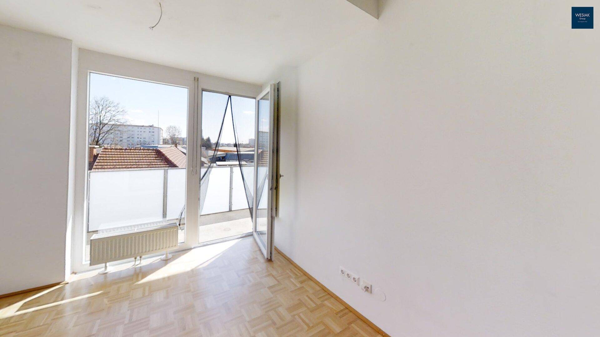 Schlafzimmer mit Parkettboden und großem Fenster, das Zugang zum Balkon bietet.
