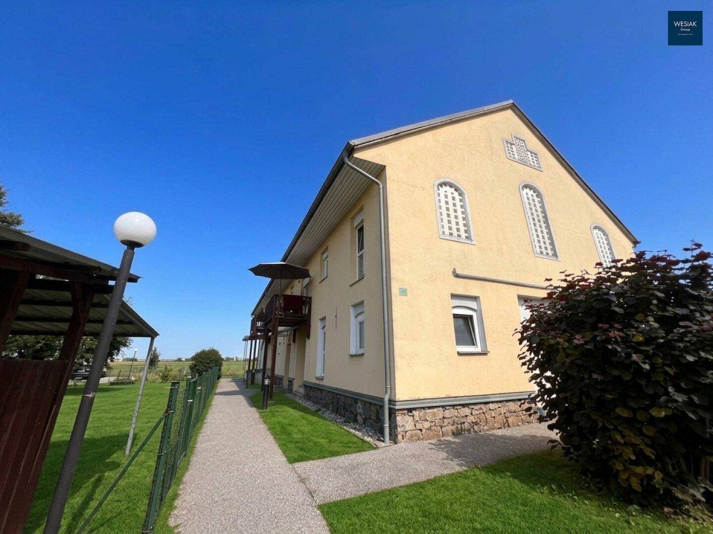 Seitenansicht des gelben Gebäudes mit Balkonen und gepflegtem Rasenbereich.
