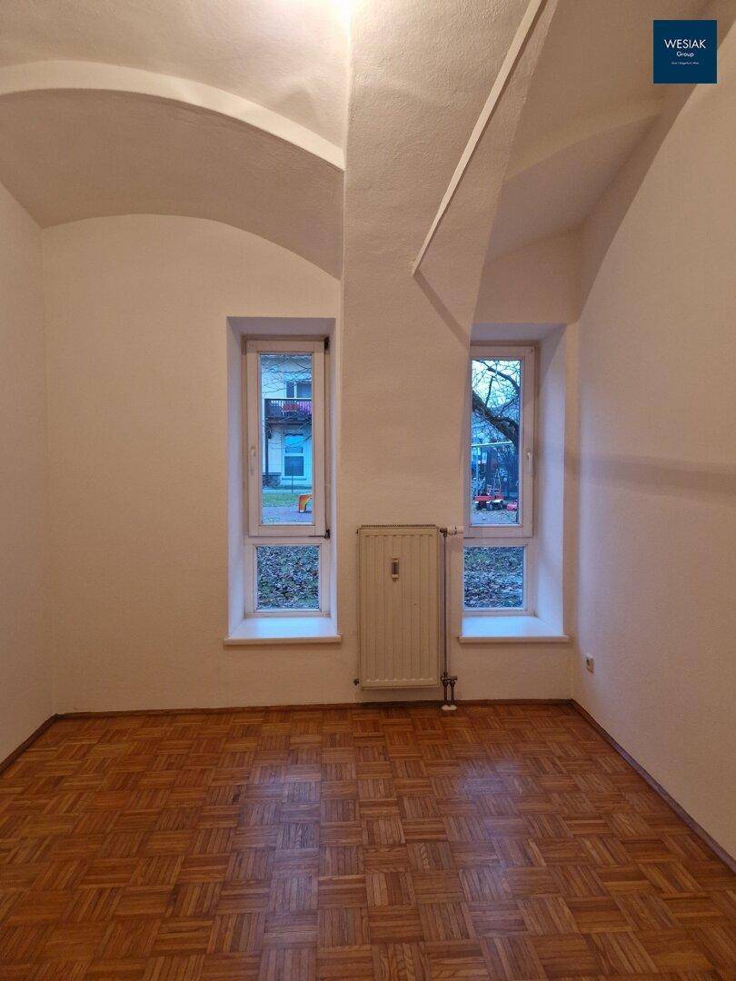 Geräumiger leerer Raum mit Gewölbedecke, Parkettboden und zwei Fenstern.