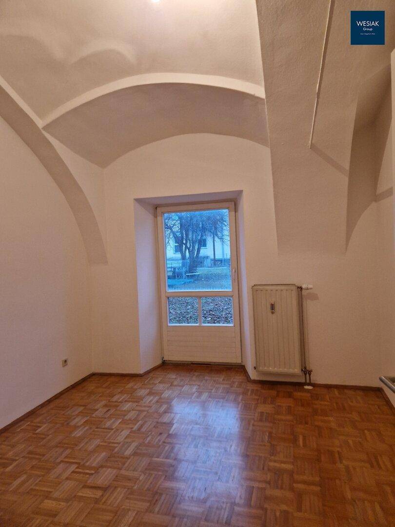Heller leerer Raum mit Gewölbedecke, Parkettboden und großem Fenster.