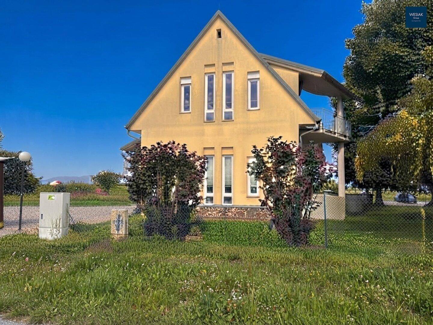 Vorderansicht des gelben Hauses mit hohen Fenstern und gepflegten Büschen im Vorgarten.