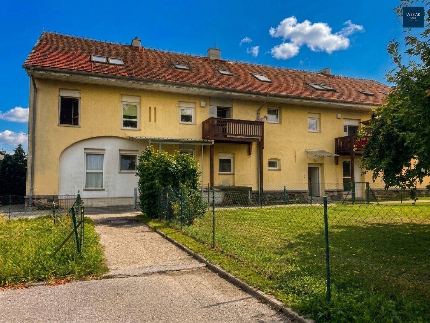 Rückseite des Gebäudes mit mehreren Balkonen und großem Gemeinschaftsgarten.