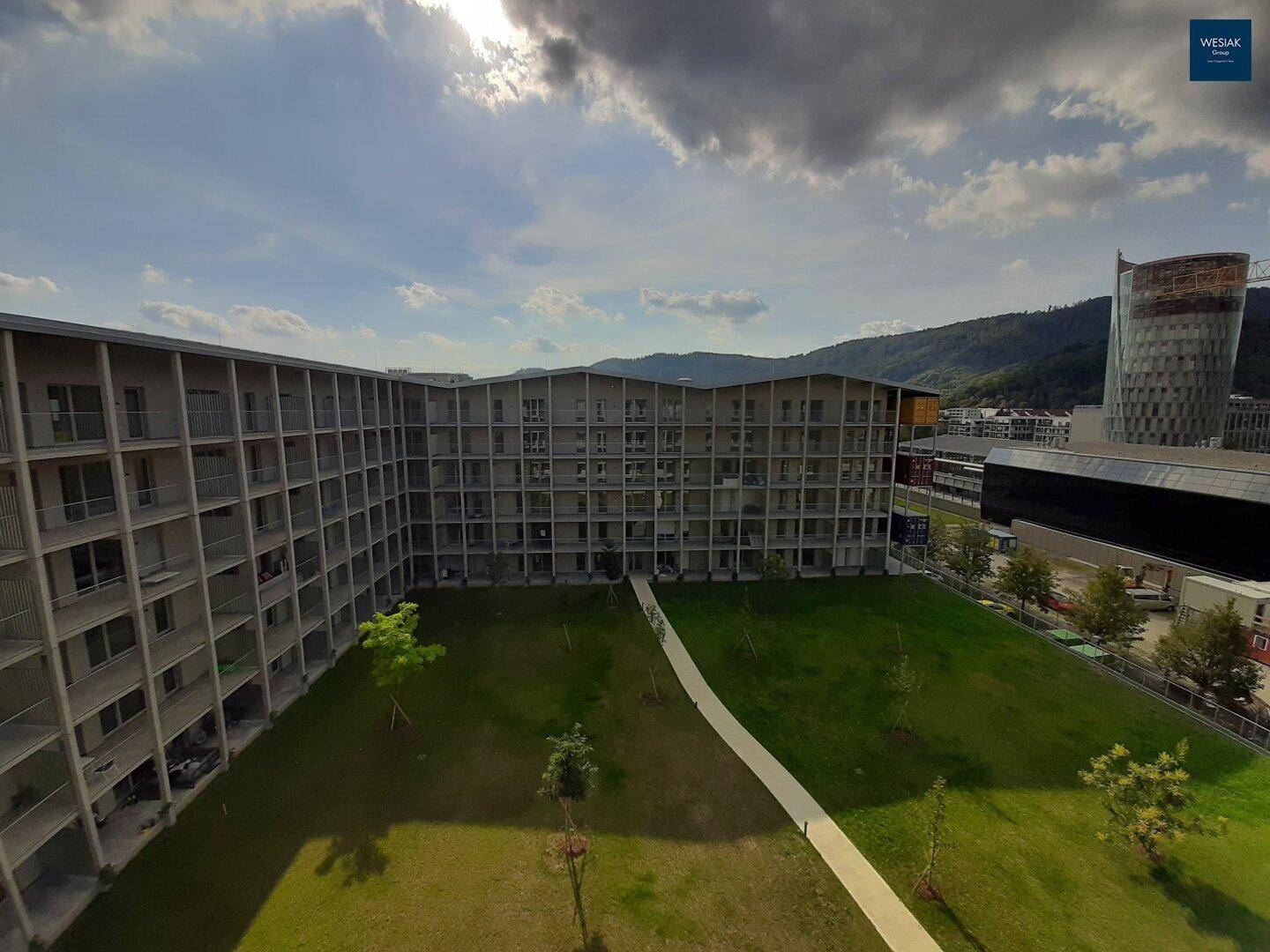 Luftaufnahme des modernen Wohnkomplexes mit Grünflächen und Bergblick im Hintergrund.