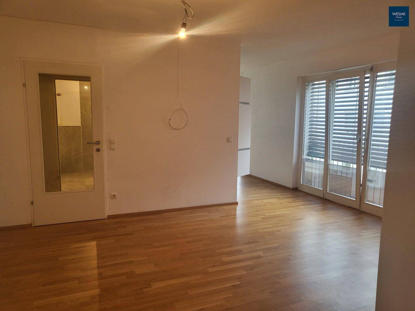 Geräumiger Wohnbereich mit Parkettboden und großen Fenstern, die viel Tageslicht hereinlassen.