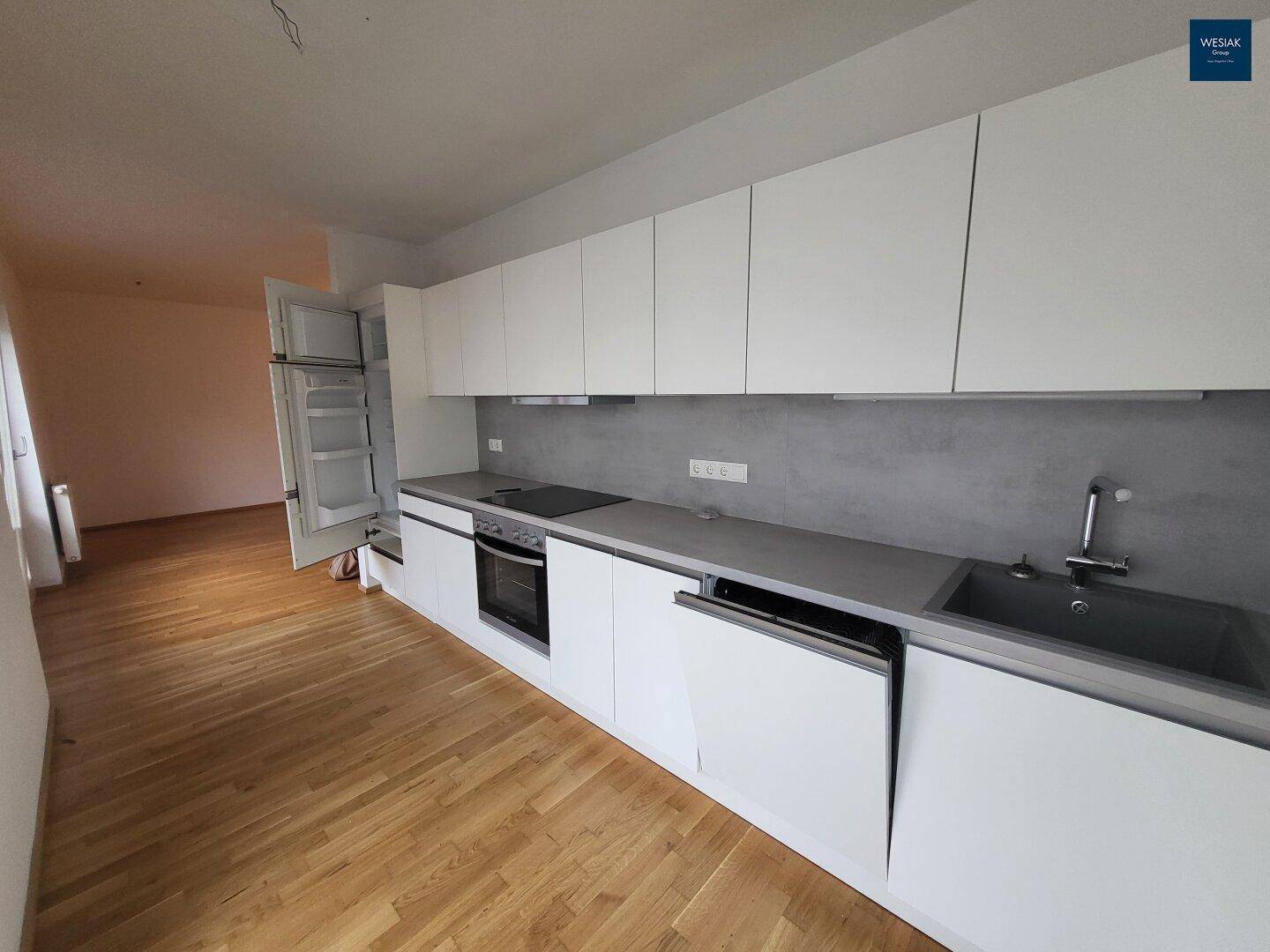 Moderne Einbauküche mit weißen Schränken, grauer Arbeitsplatte und integrierten Geräten.