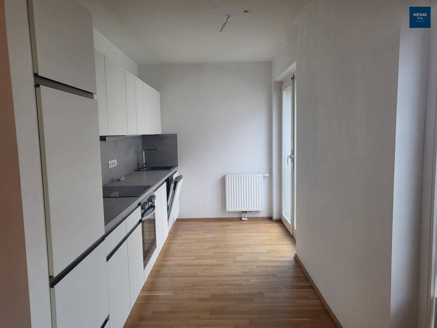 Lange, moderne Küche mit weißen Schränken, integrierten Geräten und Fenster für Tageslicht.