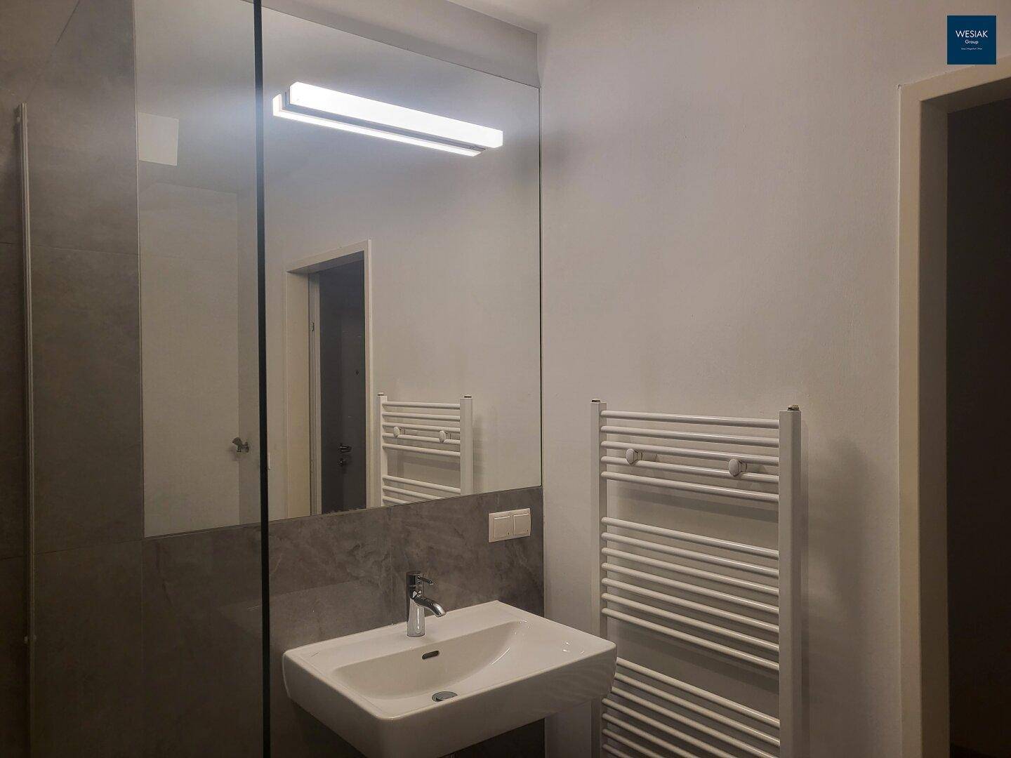 Modernes Badezimmer mit Waschbecken, großem Spiegel und beheiztem Handtuchhalter.
