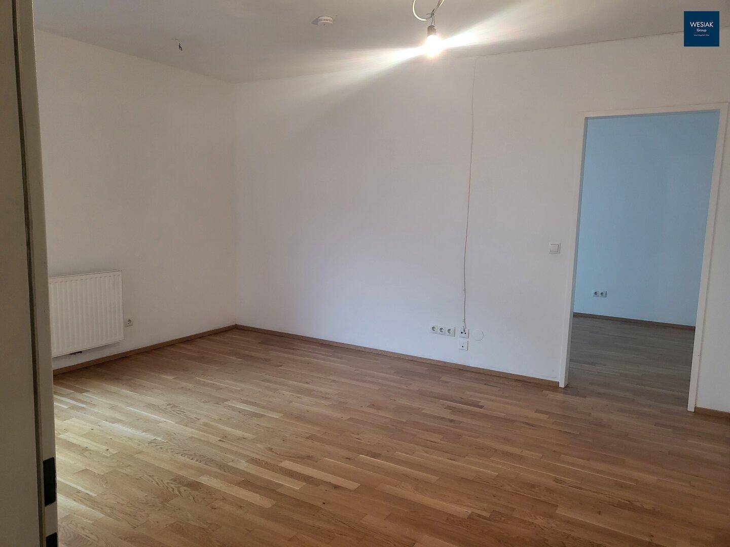 Heller Raum mit Parkettboden und weißen Wänden, angrenzend an einen Raum mit blauen Wänden.