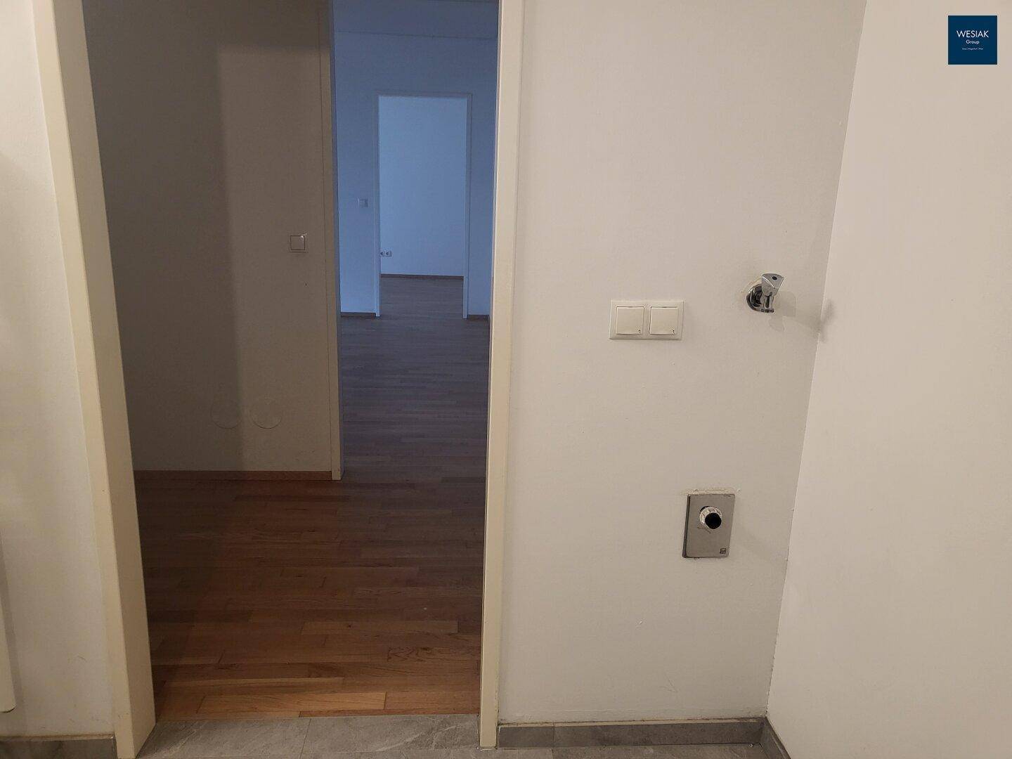 Eingangsbereich mit grauen Fliesen und Übergang zu einem Raum mit Parkettboden.