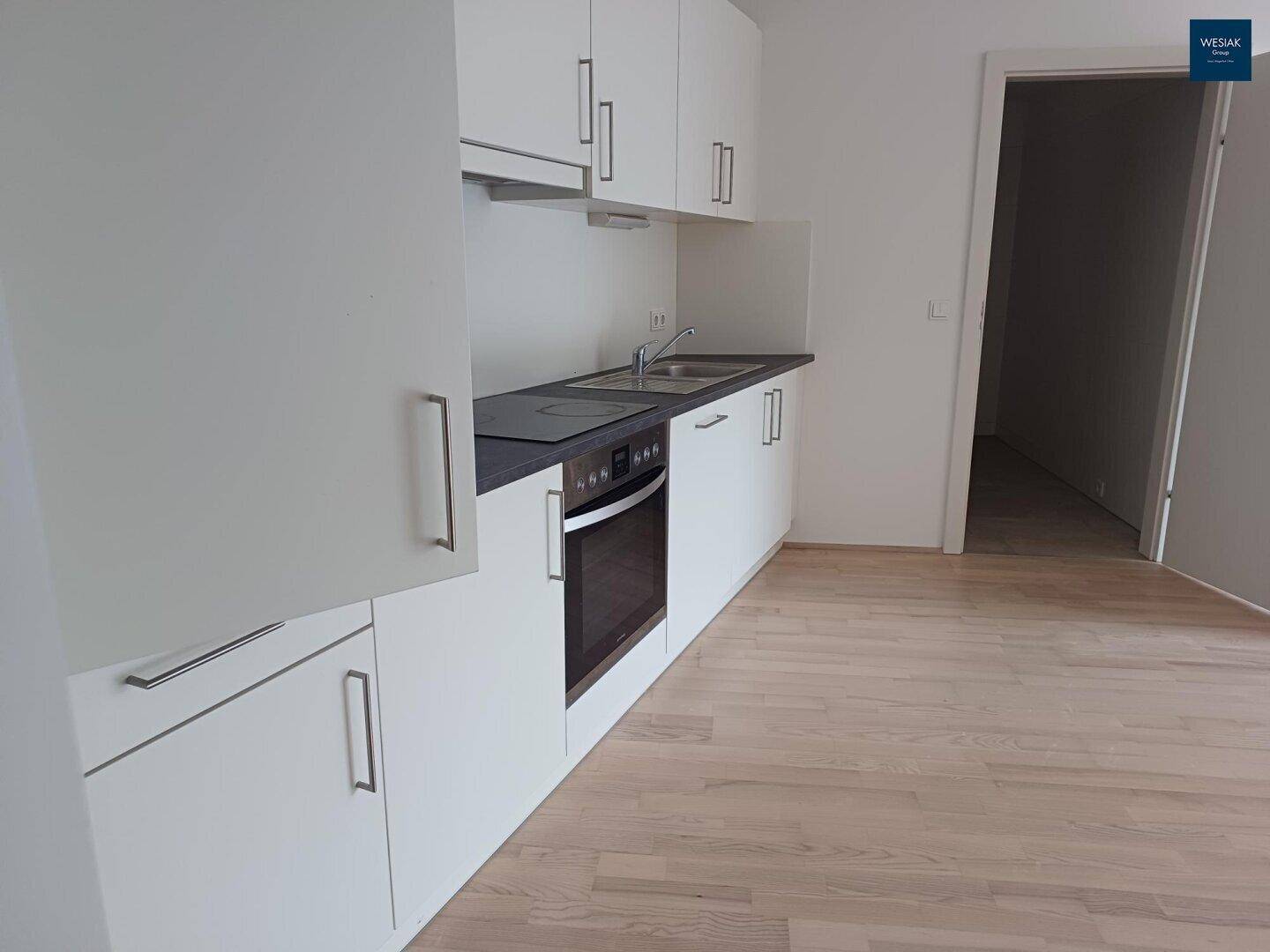 Moderne Einbauküche mit weißen Schränken, dunkler Arbeitsplatte und integriertem Backofen.