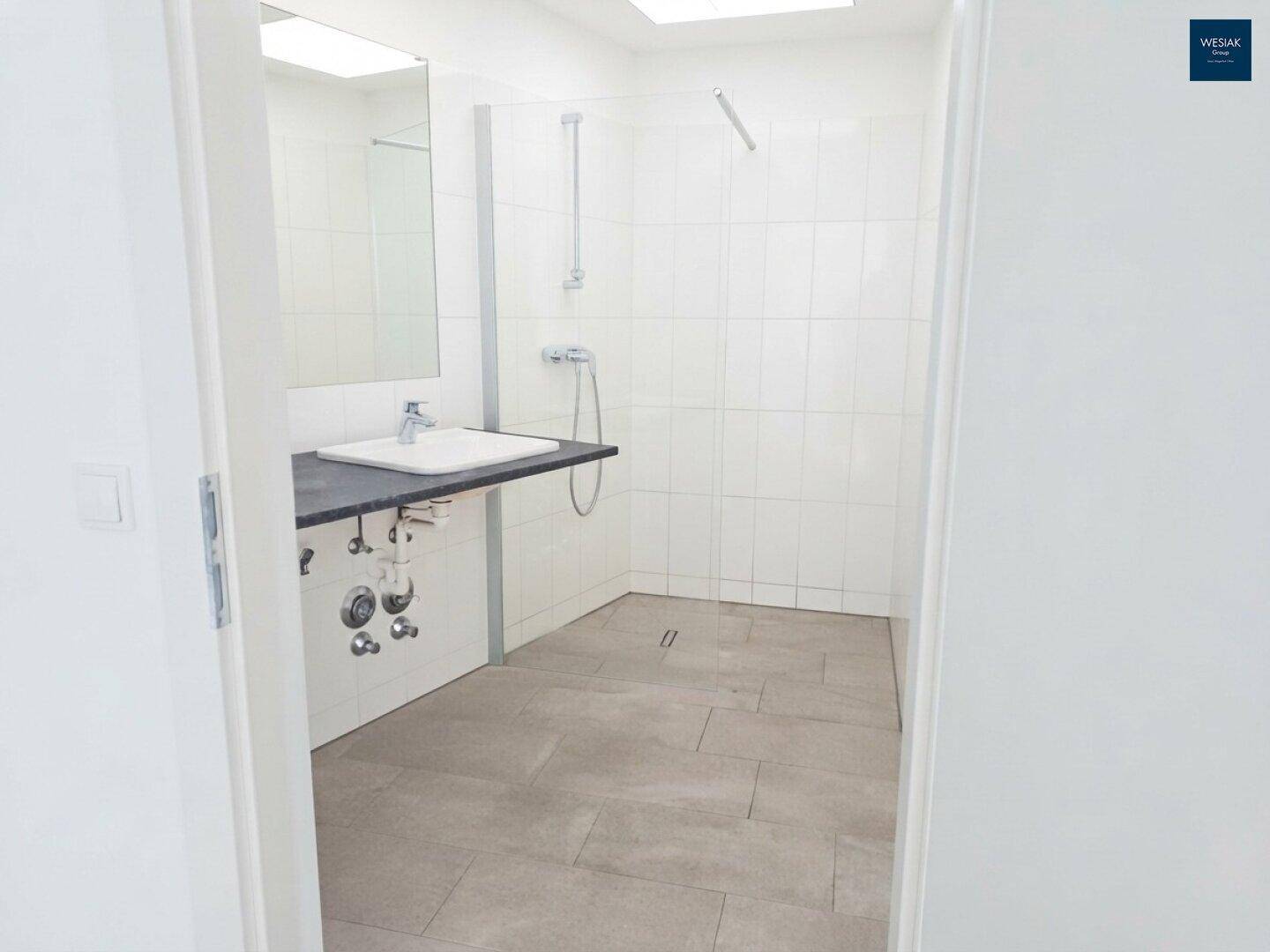 Modernes Badezimmer mit großer ebenerdiger Dusche, Fliesenboden und einem einzelnen Waschbecken.