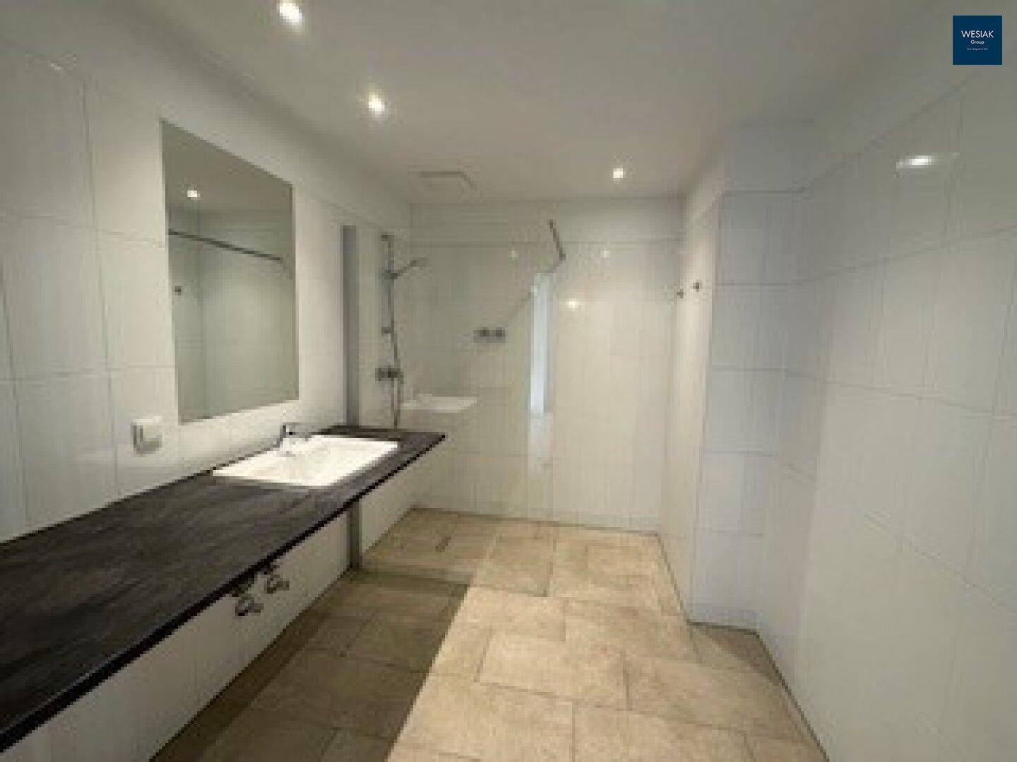Geräumiges Badezimmer mit weiß gefliesten Wänden und einer großzügigen, modernen Duschfläche.
