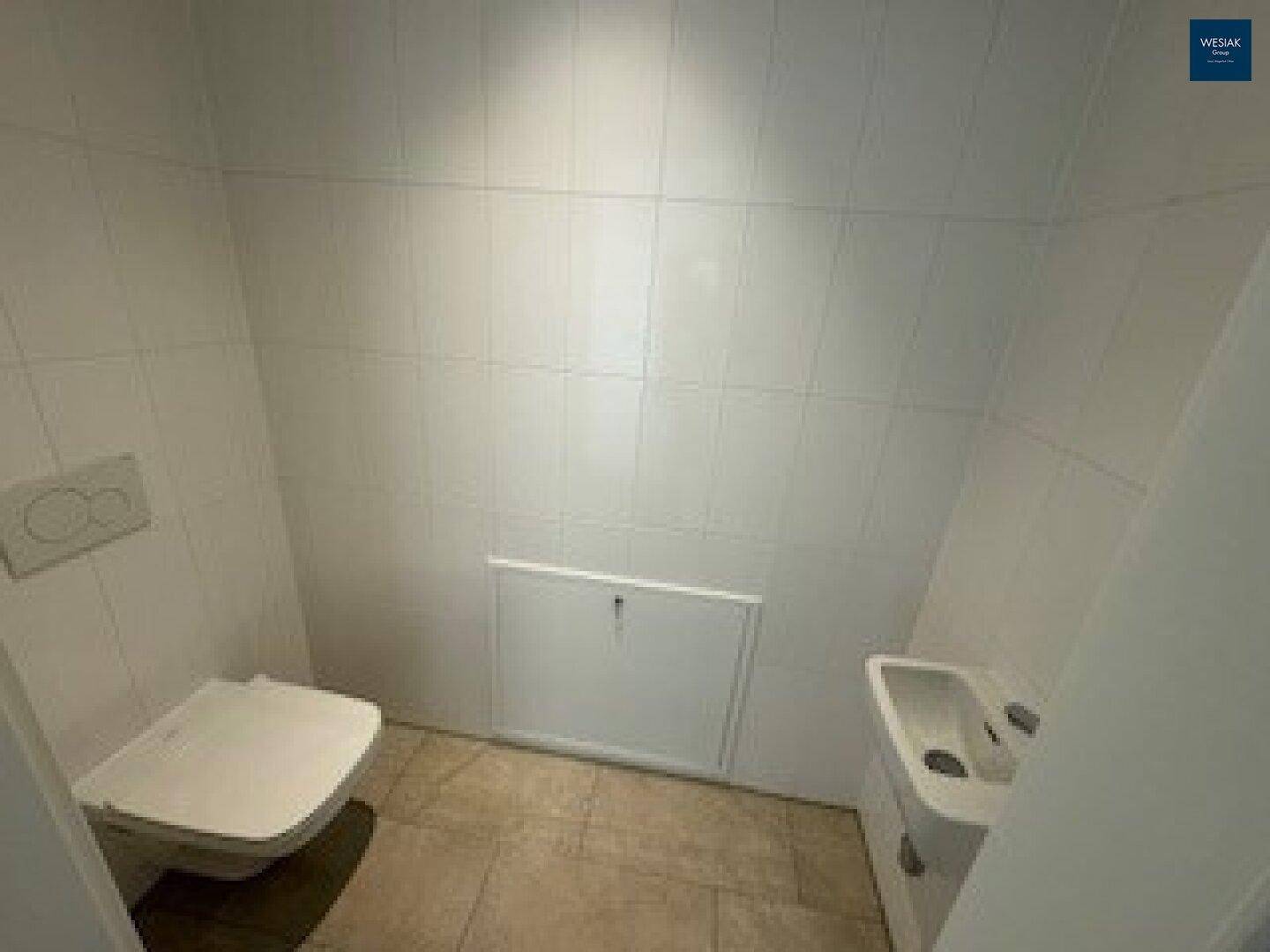 Kleines Gäste-WC mit wandhängender Toilette, kleinem Waschbecken und hellen Fliesen an Wänden und Boden.