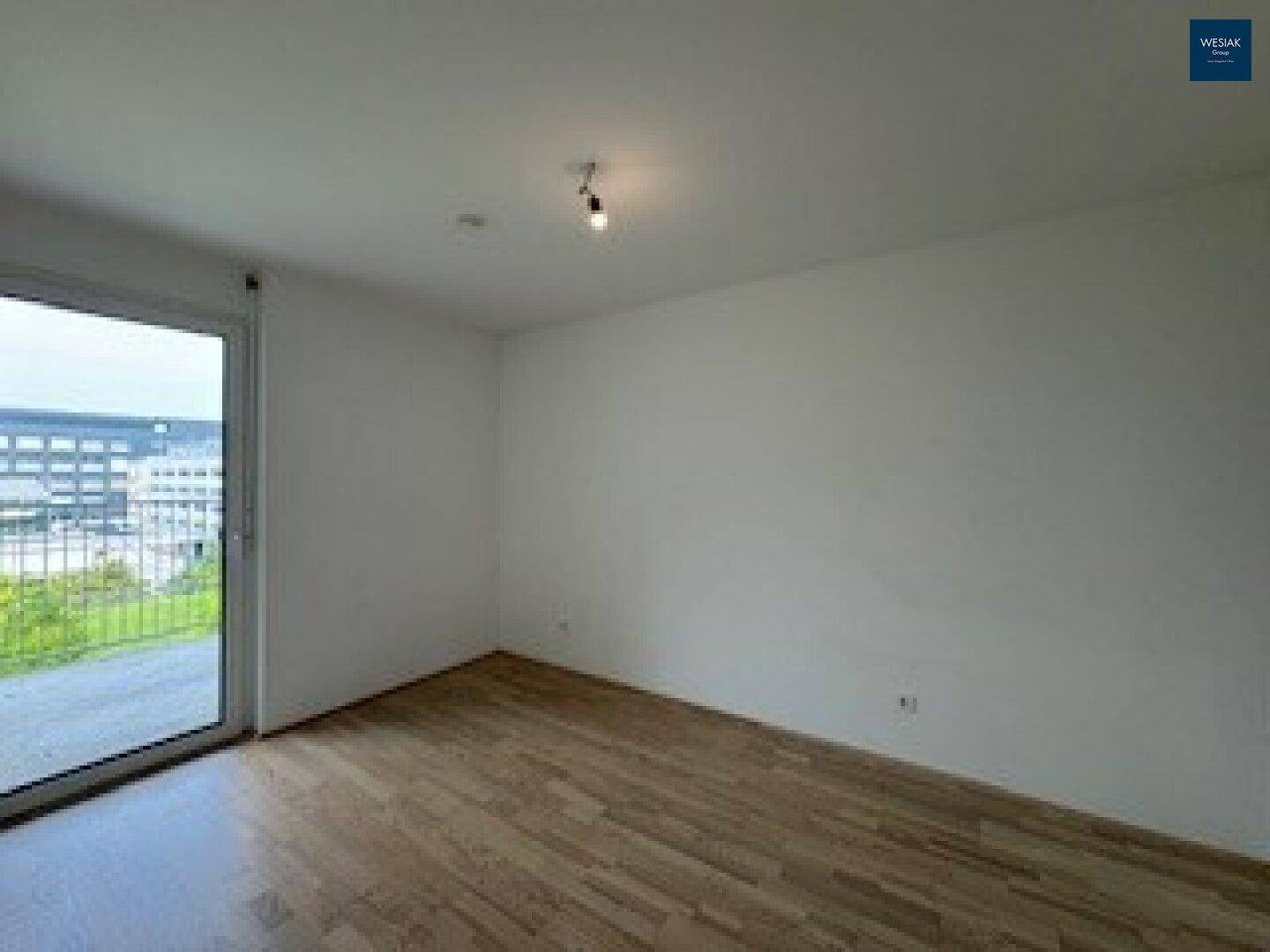 Lichtdurchflutetes Zimmer mit Parkettboden und großem Fenster, das einen weiten Blick nach draußen ermöglicht.