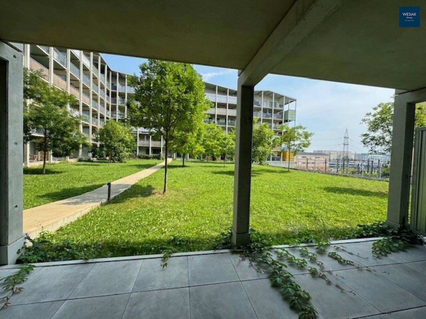 Geräumige Terrasse mit Blick auf einen großen Gemeinschaftsgarten und moderne Wohngebäude im Hintergrund.