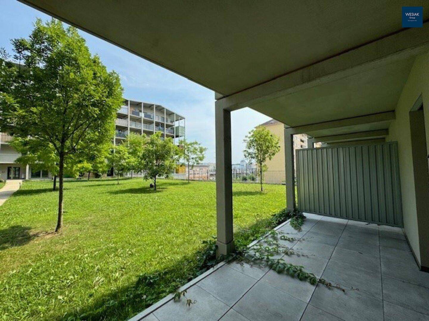 Überdachte Terrasse mit Fliesenboden und Blick auf eine weitläufige, grüne Rasenfläche mit Bäumen.